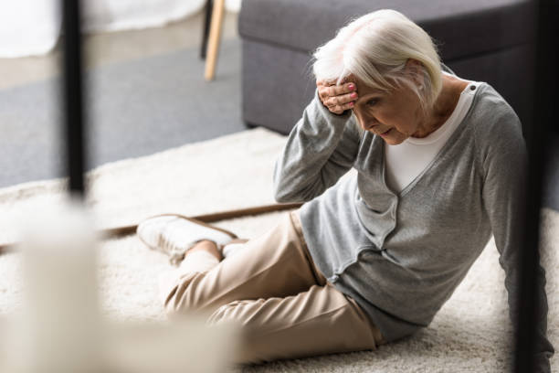 senior woman with migraine sitting on carpet and touching forehead with hand