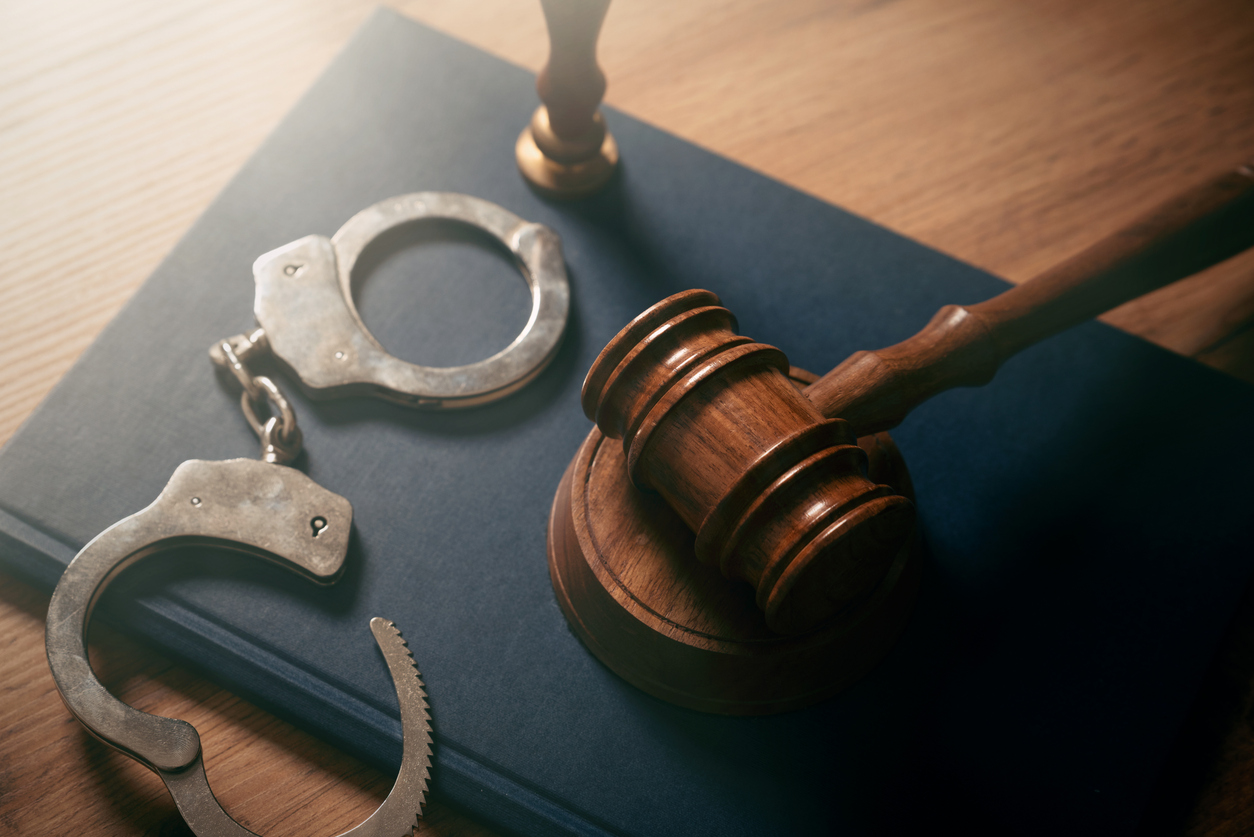 A judge's gavel next to an open pair of handcuffs.